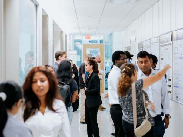 A group of students and faculty members standing in a corridor, having conversations and viewing research posters