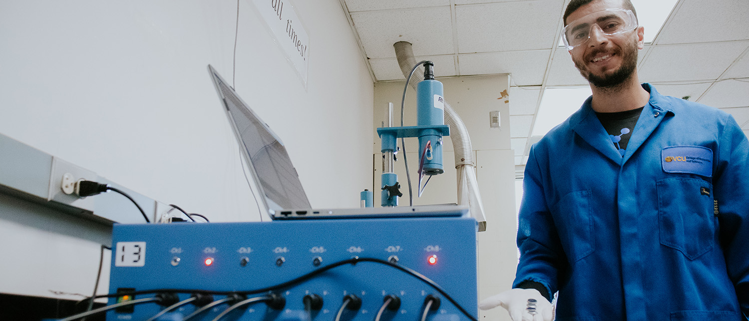 A student stands behind mechanical equipment in a chemistry lab