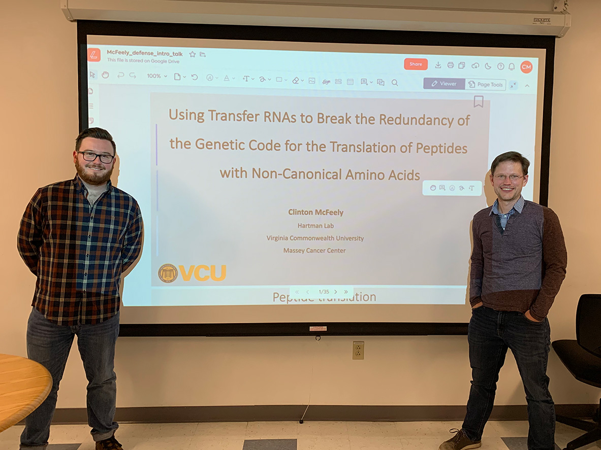 Clinton McFeely and Professor Matthew Hartman stand in front of a slideshow presentation projected onto a screen