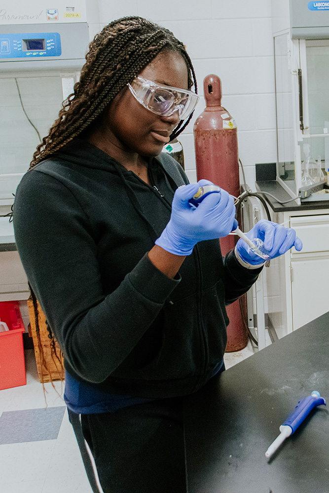 A student wearing gloves adds a substance to a vial