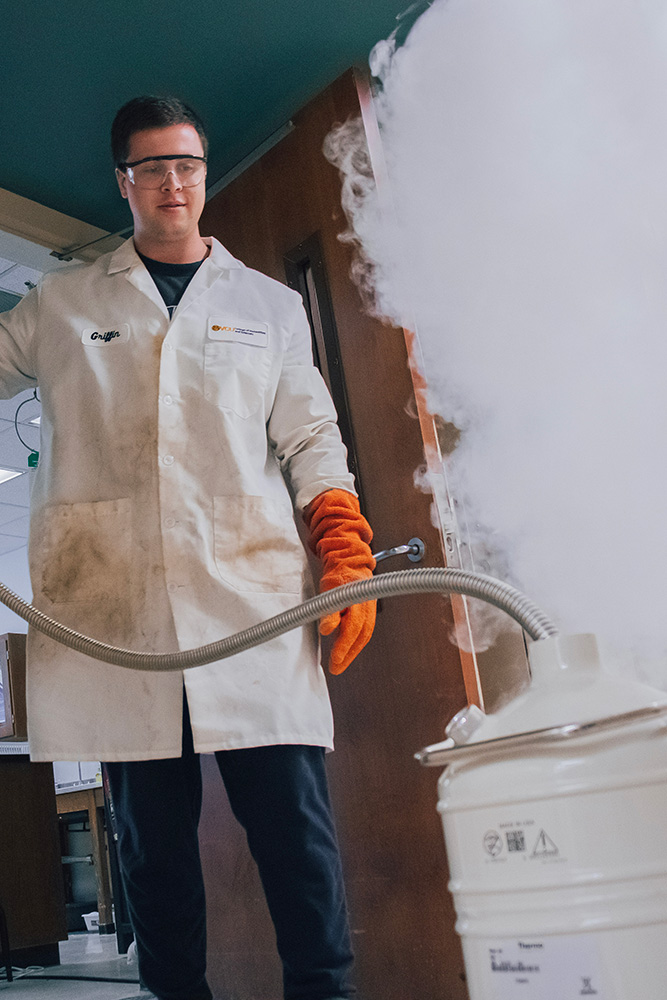 A student in a lab coat watches as a tank releases steam