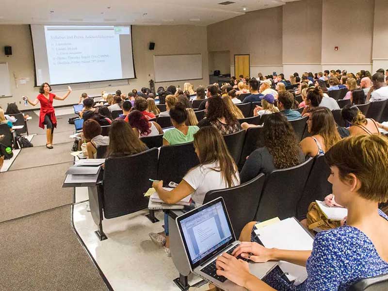 a professor teaching a large class full of students who are taking notes